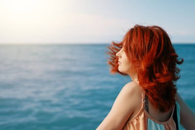 Genç bir kadın, güneşli bir günün ışıl ışıl mavi deniz özüne karşı kumsalda geriye bakar..