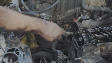 Tamirci çıplak ve kirli elleriyle sürgüyü bir cırcır ile motor mili zincirinin makara içine sıkıştırdıktan sonra 