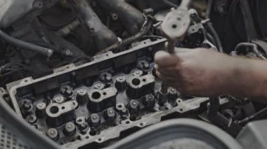 Bir otomobil atölyesinde, bir tamirci motor bileşenlerini tamir etmek için çeşitli araçlar kullanarak bir motoru tamir etmektedir.