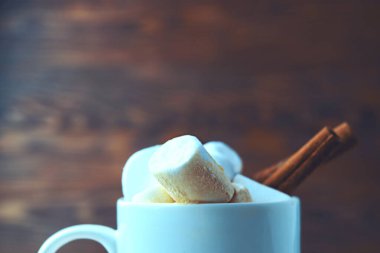 Sıcak kakaoyla dolu, kabarık şekerlemeler ve tarçın çubuğuyla süslenmiş beyaz bir fincanın yakın plan görüntüsü.