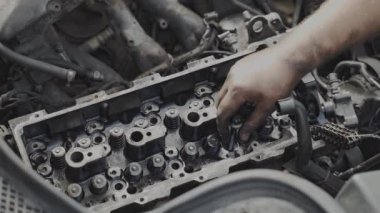 Atölyede açık bir araba motoru üzerinde çalışan bir tamircinin yakın çekimi. Araç bakımı devam ediyor.