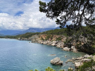 Phaselis kıyısındaki dağların ve kayaların panoramik manzarası güneşli havada Kemer yakınlarındaki Akdeniz 'in mavi ve berrak suyuyla. Antalya, Türkiye.