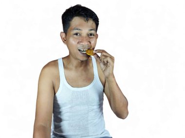 Genç Asyalı adam dişleriyle bozuk para ısırıyor. Orijinalliğini kontrol ediyor, beyaz bir arka planda izole edilmiş..