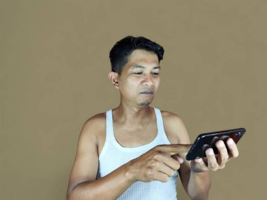 Kahverengi arka planda izole edilmiş akıllı telefondan video oyunu oynayan mutsuz Asyalı genç adam.