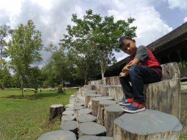 Asyalı küçük çocuk ağaç gövdesinde oturuyor.