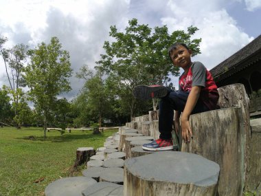 Asyalı küçük çocuk ağaç gövdesinde oturuyor.