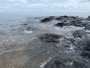 Önünde büyük bir kaya olan kayalık bir sahil. Kayalar sahile saçılmış ve Nibung Indah sahilinde su sakin.