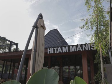 Balikpapan-Doğu Kalimantan Kasım 02.2024 Kapalı bir açık kafe terası. Dev şemsiyeli, masalı ve sandalyeli. Güneşli bir günde Hitam Manis Kafe 'de müşterileri bekliyor.