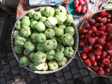 Çeşitli su elmaları gibi meyveler geleneksel bir pazarda satılık bir sepette sergilenir.