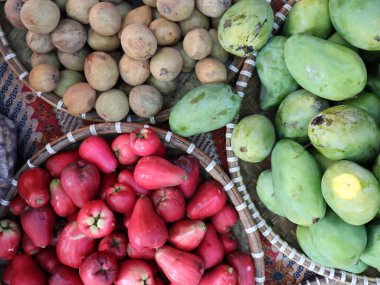 Çeşitli su elmaları gibi meyveler geleneksel bir pazarda satılık bir sepette sergilenir.