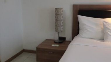 Cikarang-West Java 19 Kasım 2024 Geniş bir otel odası beyaz çarşaflı, çevre aydınlatmalı ve sofistike dekorlu büyük bir yatak. Lüks bir koltuk ve şık bir halı içerir..