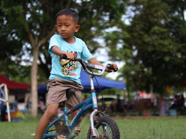 Balikpapan-Doğu Kalimantan 30 Kasım 2024 bisiklete binen çocuk, 5 yaşındaki mutlu çocuk güzel bir sonbahar gününde bisikletle bahar parkında eğleniyor.. 