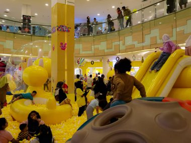 29 Aralık 2024 'te Balikpapan çocuk parkında bir sürü topla oynayan mutlu çocukların resmi. Çocuk, sarı nüanslarla oyun bahçesinde banyo topu (mandi bola) oynuyor.