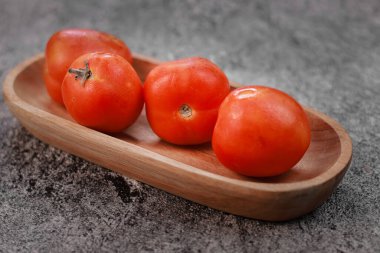 Dikdörtgen ahşap bir kasede dört taze kırmızı domates.