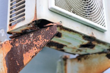 Eski paslı klima dış ünitesi. Duvara paslı bir parantez takılmış. Seçici bir odak noktası var.