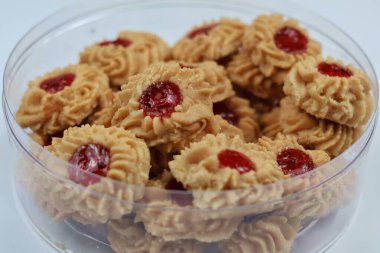 Beyaz arkaplanda izole edilmiş şeffaf plastik mika kabın içinde Çilek Reçelli Kue Semprit veya Tereyağlı Kurabiyeler.