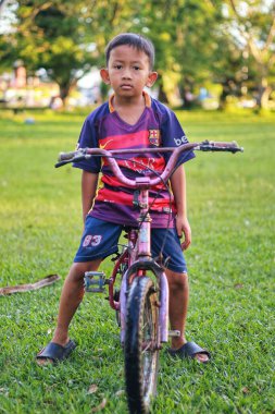 Balikpapan-Endonezya 12 Nisan 2025 Asyalı küçük çocuk parkta eski bir bisikletle futbol forması giyiyor..