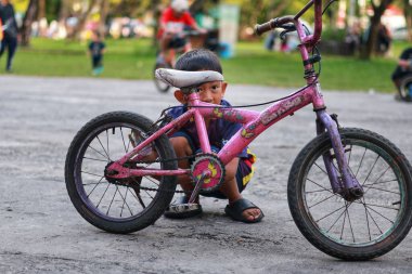 Balikpapan-Endonezya 12 Nisan 2025 Asyalı küçük çocuk parkta eski bir bisikletle futbol forması giyiyor..