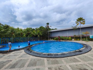 26 Nisan 2025 Balikpapan-Endonezya yüzme havuzu, yapay çim, taş patika, ağaçlar ve sandalyeli modern bir evin arka bahçesi..