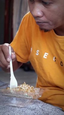 Balikpapan-Endonezya 3 Mayıs 2025 Asyalı adam şeffaf bir kutuda tavuk ve sebzeyle erişte yiyor. Siyah masada. Yemek kavramı..