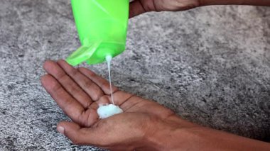 Elinde yeşil bir şampuan şişesi tutarken, Gri arka plandaki kremalı mavi kremi dök..