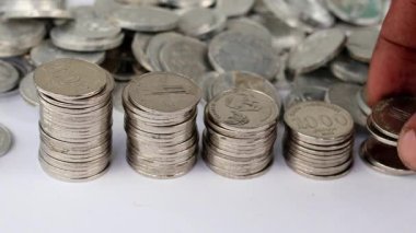 Bozuk paraları farklı yüksekliklerde istifleme, para biriktirme kavramı, daha önce erkek elinin belirlediği para yığını büyüyen iş, beyaz masanın üzerine para yığan genç adam..