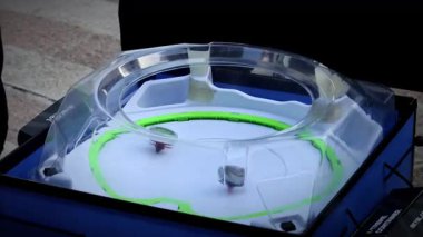 Bir çocuk beyblade marşını beyaz arenanın yukarısında birlikte Bayblade oynayan çocuklarla birlikte tutar. Beyblade 'ler küçük burunlu metal kaplamalardır..