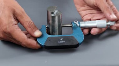 El ele tutuşan analog mikrometre ya da diff mikrometre kalite kontrol yuvarlaklık gezegeni gri masa üzerinde döndürür. Vida ölçer kalibreleri analogu kullan. kalite kontrol kavramı.