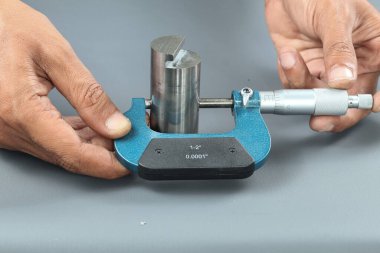 El ele tutuşan analog mikrometre ya da diff mikrometre kalite kontrol yuvarlaklık gezegeni gri masa üzerinde döndürür. Vida ölçer kalibreleri analogu kullan. kalite kontrol kavramı.