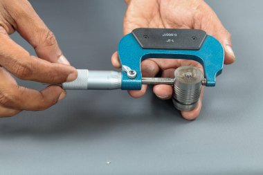 El ele tutuşan analog mikrometre ya da diff mikrometre kalite kontrol yuvarlaklık büyüsü kapakçığı gri masanın üzerinde. Vida ölçer kalibreleri analogu kullan. kalite kontrol kavramı.