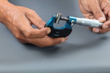 El ele tutuşan analog mikrometre ya da diff mikrometre kalite kontrol tüpü gri masanın üzerinde. Vida ölçer kalibreleri analogu kullan. kalite kontrol kavramı.