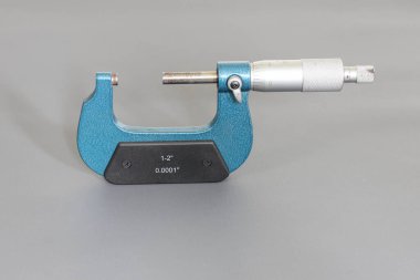 Gri arkaplanda izole edilmiş mavi bir mikrometre, bir nesnenin dış çapını ve uzunluğunu (kalınlığını) kıskaçlayarak ölçmek için kullanılan bir araçtır..