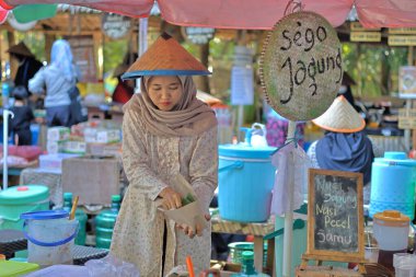 Balikpapan-Endonezya 29 Mayıs 2025 Geleneksel Cava kıyafetleri ve pelerinli kız (Cava şapkası) Geleneksel bir pazarda müşterilere hizmet veriyor