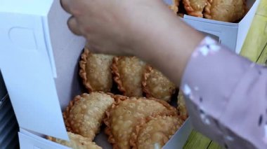 Bir jalangkote (Jalangkote, Endonezya 'dan gelen ve malzemelerin karışımıyla dolu kızarmış hamur kabuğuyla tanınan popüler bir atıştırmalıktır) satıcı, bir kağıt kutuya jalangkote koyup alıcıya servis yapmaktadır.