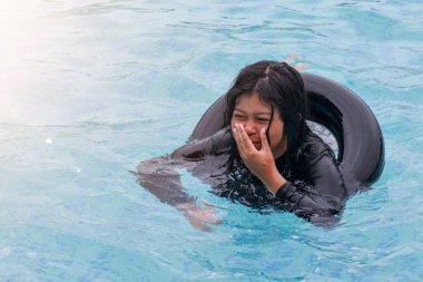 Asyalı genç yüzme havuzunda yüzerken arabanın iç borularından çıkan şamandıraları kullanarak mutlu görünüyor..