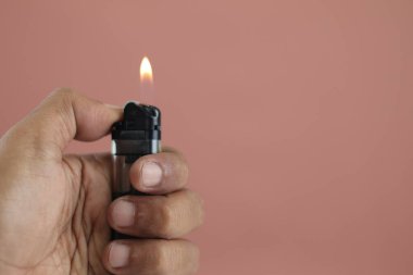Balikpapan-Indonesia June 20, 2025 Hand holding a burning lighter, isolated on brown background, Close up hand holding burning gas lighter. 