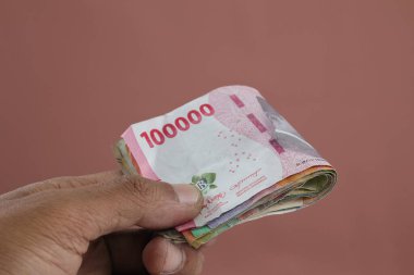 Mali gelir için Endonezya Rupiah 'ı ya da izole edilmiş arka planda online hizmeti erkek elinde tutuyor. Silah çok para tutuyor, büyük kar..