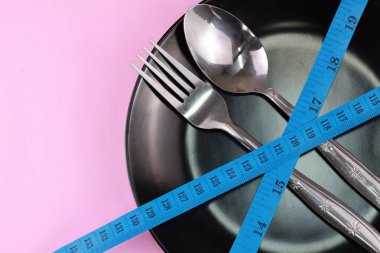 Sağlıklı beslenme veya beslenme konsepti. Çatal ve kaşık, boş tabağa sarılı mavi mezura. izole arkaplan.