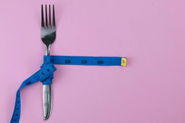 Pembe arka planda mavi şeritli paslanmaz çatal var. Diyet ve vücut konsepti. Boşluğu kopyala.