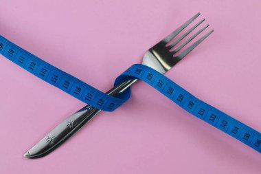 Pembe arka planda mavi şeritli paslanmaz çatal var. Diyet ve vücut konsepti. Boşluğu kopyala.