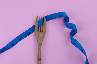 Ahşap çatal, bükülmüş mavi bant ile bağlanmış. Pembe arka planda izole edilmiş. Diyet ve vücut kavramını kopyalama alanı ile uydur.