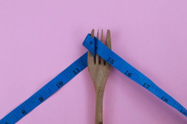 Ahşap çatal, bükülmüş mavi bant ile bağlanmış. Pembe arka planda izole edilmiş. Diyet ve vücut kavramını kopyalama alanı ile uydur.