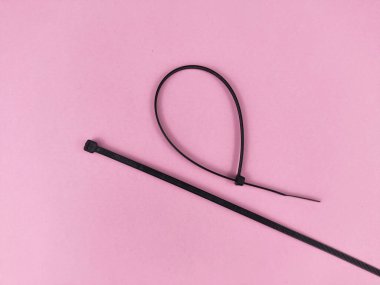 Siyah kablo bağı ya da esnek kendini kilitleyen plastik fermuar pembe arka planda izole edilmiş. Farklı boyutlarda, uzun, kumaş ve renklerde..
