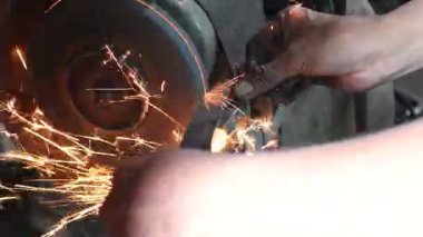 Metal yapımında el değirmencisiyle çalışan bir işçi. Fabrikadaki çelik yapının elektrik tekerlekleri gıcırdıyor. Bıçak keskinleştirme