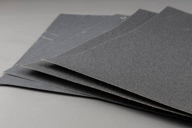 Gri arkaplanda zımpara kağıdını kapat. Zımpara kağıdındaki kum taneleri görülebilir ve zımpara kağıdındaki kabalık seviyesi kum tanelerinin inceliğini gösterir..