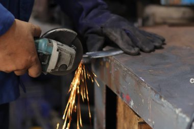 Öğütücü kullanarak tabak kesen bir adamın elini kapatmak imalat atölyesinde kıvılcımlar yaratır. Sanayi