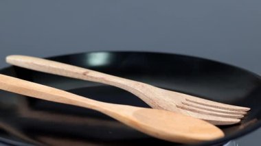 Tahta kaşık ve çatal siyah seramik tabakta. 4k dönüşlü ekran. Sağlıklı yaşam konsepti.
