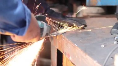 Öğütücü kullanarak tabak kesen bir adamın elini kapatmak imalat atölyesinde kıvılcımlar yaratır. Sanayi