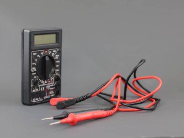 Voltajı ölçmek için sondaları olan siyah dijital multimetre, gri arkaplanda direnç, multimetre elektronik bir ölçüm aletidir..