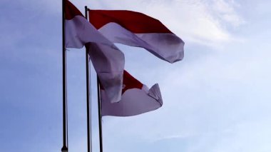 Endonezya bayrağı rüzgâr tarafından dalgalanan bir direkte mavi gökyüzü ve bulutlardan oluşan bir arka planda dalgalanıyor. Ulusal gurur ve bağımsızlığı sembolize ediyor. alçak açı ve arka planda yumuşak gün ışığı.